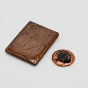 A tiny leather-bound book next to a penny for scale.